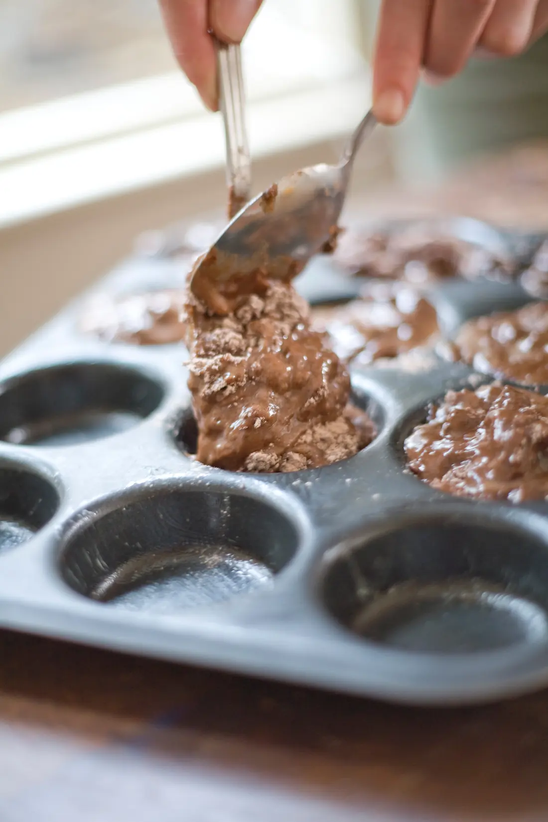 Spooning chocolate muffin mixture into a muffin tin